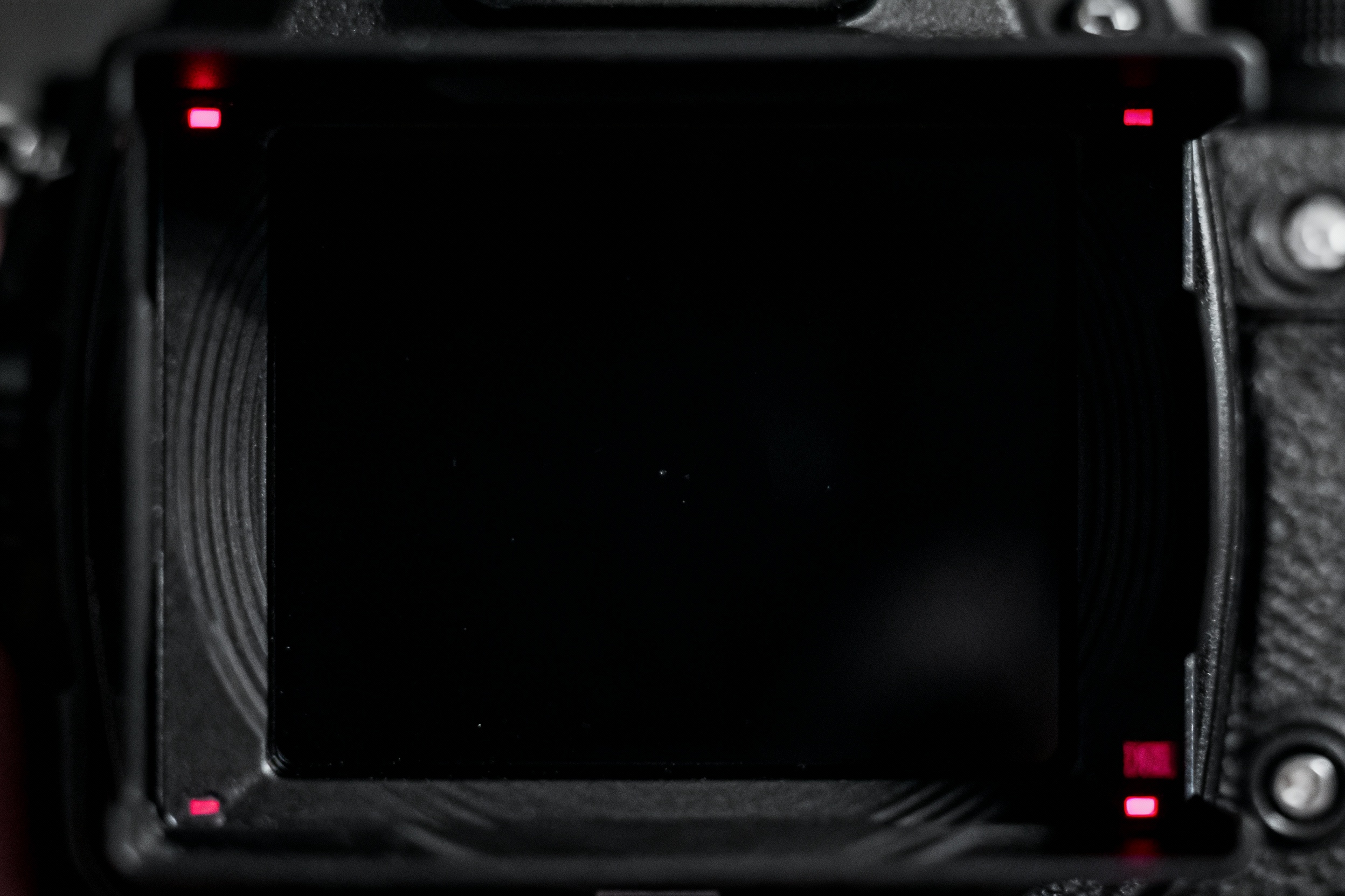 A close-up of a camera’s viewfinder displaying a pitch-black scene with only faint red indicator lights visible, illustrating the disorienting experience of framing and focusing in zero-light conditions.
